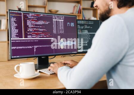 Cropped image of unshaven programmer man wearing eyeglasses working with computers in office Stock Photo