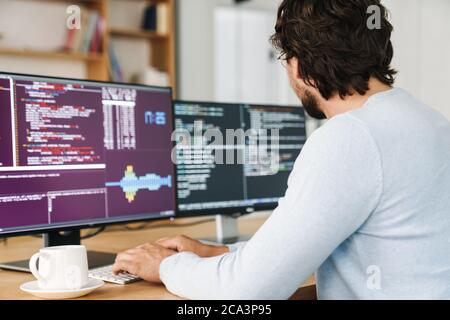 Cropped image of unshaven programmer man wearing eyeglasses working with computers in office Stock Photo