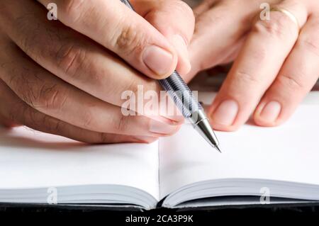 The right hand of a man writing with a pen on a notebook with blank pages. Journalistic or creative activity. White pages. Stock Photo