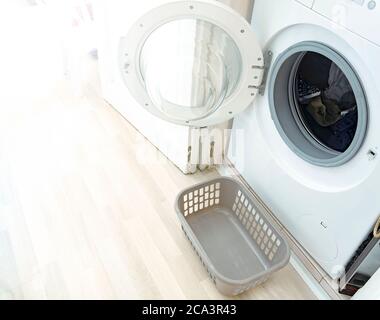 a washing machine with the door open and a small plastic basket to hold the freshly washed laundry. Interior of a house. Household chores and cleaning Stock Photo