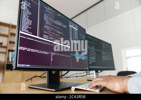 Cropped image of programmer man typing on keyboard while working with computers in office Stock Photo