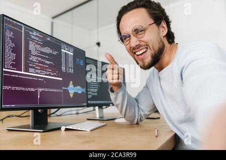 Image of excited caucasian programmer man pointing finger at camera while working with computers in office Stock Photo