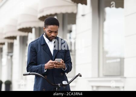 Handsome businessman texting on phone sitting on bike Stock Photo