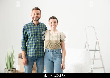 Portrait of happy beautiful young couple embracing each other in new empty flat with moving stuff Stock Photo
