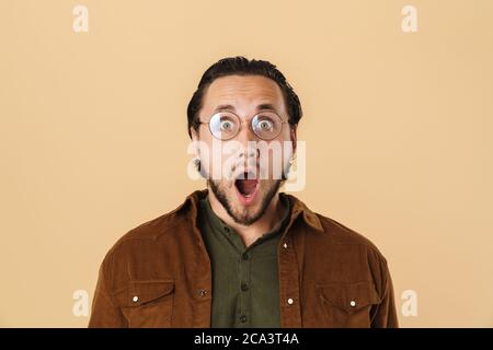 Image of handsome shocked man in eyeglasses expressing surprise at camera isolated over beige background Stock Photo