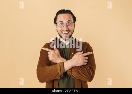 Image of bearded excited man in eyeglasses pointing fingers aside isolated over beige background Stock Photo