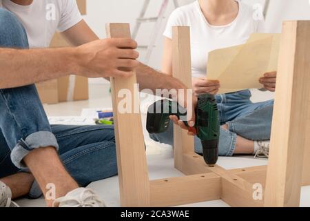 Close-up of unrecognizable man sitting on floor and using screwdriver while assembling table with wife Stock Photo