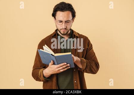 Image of serious unshaven man in eyeglasses reading book isolated over beige background Stock Photo