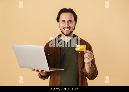 Image of excited bearded man holding credit card and notebook isolated over beige background Stock Photo