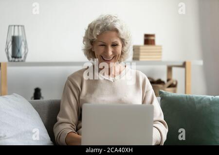 Elderly woman working texting message on laptop sit on couch Stock Photo