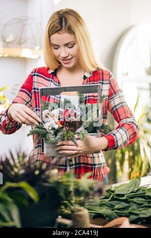 young caucasian florist at work, pretty young blond female making fashion modern bouquet of different flowers wearing red casual shirt Stock Photo