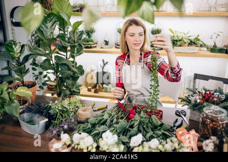 charming beautiful happy young florist woman standing in greenhouse full of flowers and plants, enjoy working with botany Stock Photo