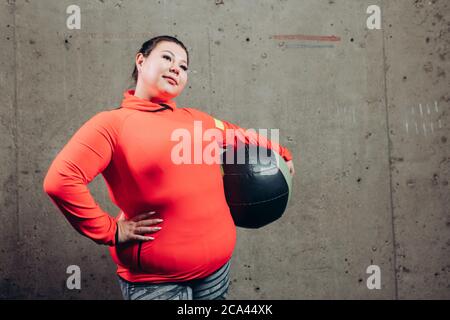 positive plump woman in stylish sportswear holding leather ball and looking at the camera. close up photo. copy space. interest Stock Photo