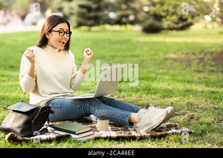 Excited asian female student reading good news sitting at park Stock Photo