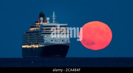 Bournemouth, UK. 3rd August 2020.  The full moon of August, sometimes known as the Sturgeon Moon, rises behind the Cunard Line cruise ship Queen Elizabeth at anchor in Poole Bay off Bournemouth Beach. credit: Richard Crease/Alamy Live News Stock Photo