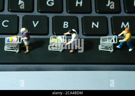 Online shop concept. Group of people walking above keyboard with cart, to avoid coronavirus. Miniature people figurines toys photography. Stock Photo