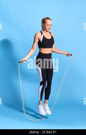 slim lovely girl in stylish sportswear enjoying skipping. full length photo. isolated blue background. Stock Photo