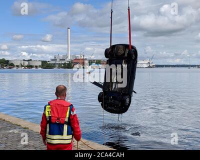 Flensburg, Germany. 04th Aug, 2020. Emergency fire brigade units use a crane to rescue a vehicle from the port basin. To escape a police check, the driver of a small car drove into a port basin in Flensburg. The drunk man had attracted the attention of the officers during the night to Tuesday because of his driving and should be checked at a parking lot near the edge of the harbor. Credit: Heiko Thomsen/Westküsten-News/dpa/Alamy Live News Stock Photo