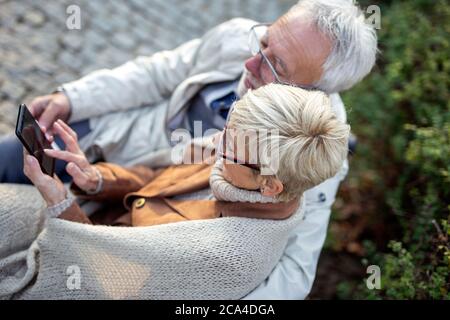 Aged man and woman with mobile on hand in park Stock Photo