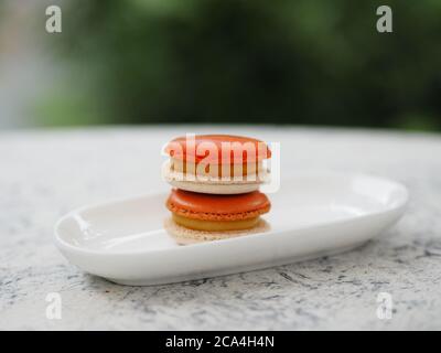 Macaron orange color in white plate shape ellipse, Dessert snacks Afternoon on marble table Stock Photo