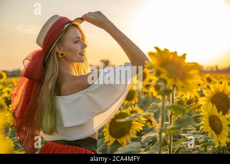 Portrait of young, happy blonde hair girl is standing in a sunflower field. Stock Photo