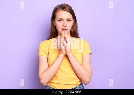 Photo of pleasant looking sad girl keeping palms together in praying gesture, whispering something, waiting for qualifying exam results, looking in ca Stock Photo