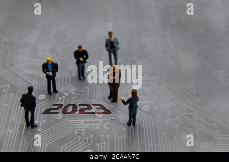 Miniature figurines posed as business people in a meeting over abstract futuristic circuit board with text year 2023