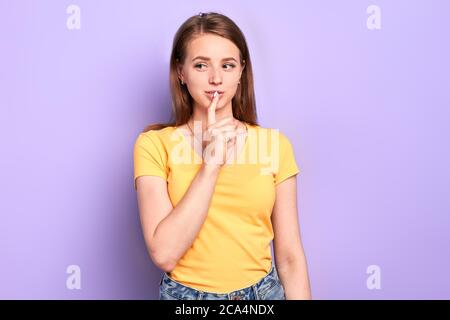 Female student with appealing appearance standing thoughtfully, holds index finger near her lips, thinking about future dreamfully, looks aside, has d Stock Photo