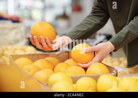 Close-up of unrecognizable woman in sweater comparing oranges while buying it at food market Stock Photo