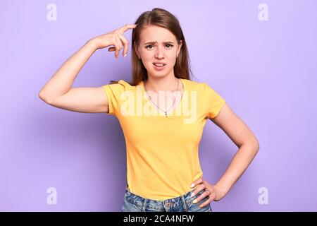 Front view of displeased clueless young woman looks with puzzlement expression, scratches head, frowning, unpleasant expression, thinks how to solve p Stock Photo