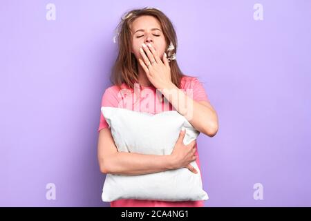 Isolated shot of tired young female with closed eyes and feathers in messy hair, covers mouth with hand yawning, feels exhausted, wants to sleep, hold Stock Photo