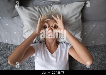 Elderly woman lying in bed looking through fingers glasses shape Stock Photo