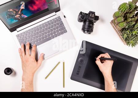 Photographer and graphic designer works on laptop. Flat lay top view of man working on photos in computer. Desk with laptop, camera and hands. Stock Photo