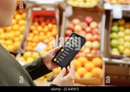 Over shoulder view of woman reading food product list on smartphone while making purchases at organic food market Stock Photo