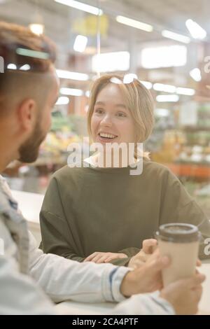 Positive young couple sitting in cafe and chatting while drinking coffee together Stock Photo