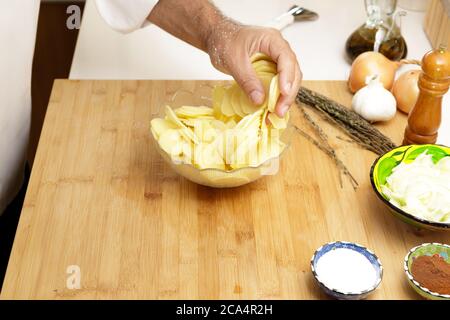 A dding salt to sliced potatoes in the kitchen Stock Photo