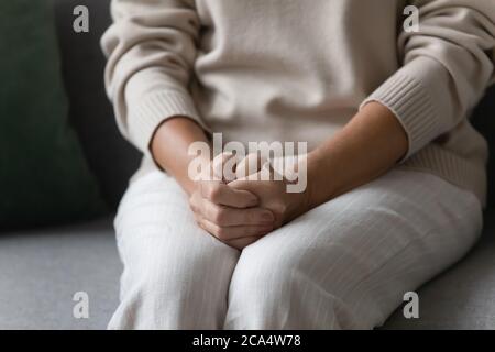 Lonely elderly woman put hands on laps sitting on couch Stock Photo