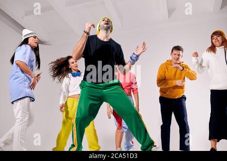 concentrated on dancing young slim man in sportswear, bending head back, looking up, raising fists up, having pleasure by dancing, preparing to concer Stock Photo