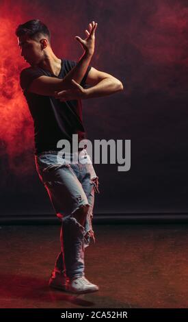 Young man professional dancer fond of dancing. dancing movements by caucasian man isolated in studio with red smoky background Stock Photo
