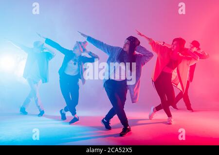 Group of diverse young hip-hop dancers in studio with special lighting effects in blue and pink colores Stock Photo