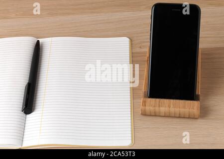 a empty lined pages of notebook opened with black pen in the middle lying, a black phone on a stand with a black screen, minimalistic clean working place, space to make plans, write down new ideas Stock Photo