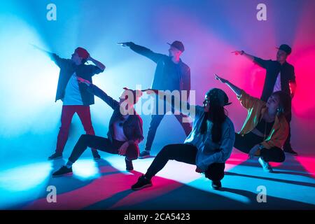 Group of diverse young hip-hop dancers in studio with special lighting effects in blue and pink colores Stock Photo