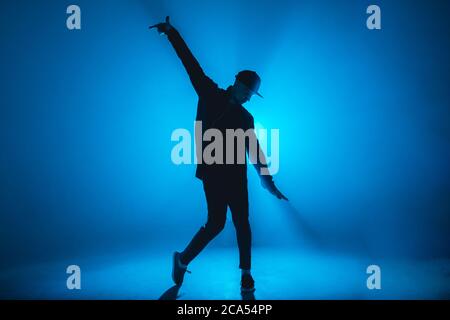 Full-size of silhouette of male break dancer performing on blue neon stage his expressive dance, Dark blue background with light flare on background Stock Photo