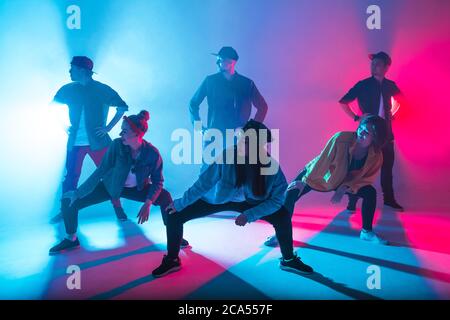 Group of diverse young hip-hop dancers in studio with special lighting effects in blue and pink colores Stock Photo