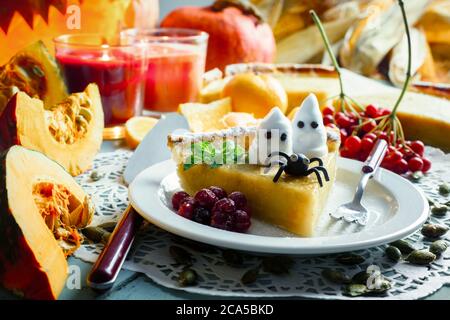 Homemade halloween pumpkin cake with black spider and small ghosts on white plate closeup. Candles and Jack-o-lantern on background. Traditional holiday food Stock Photo