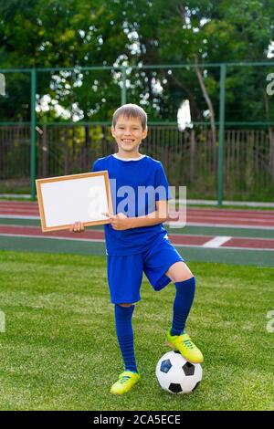 a small soccer player with a ball stands on a green soccer field with a white piece of writing paper Stock Photo