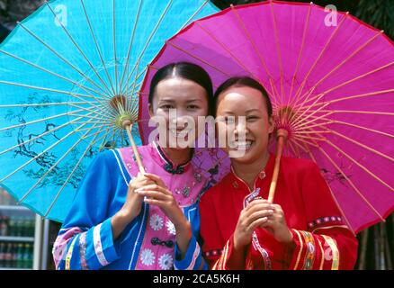 Two Smiling Young woman wearing traditional Chinese clothing, holding parasol in a park, Yunnan, China Stock Photo