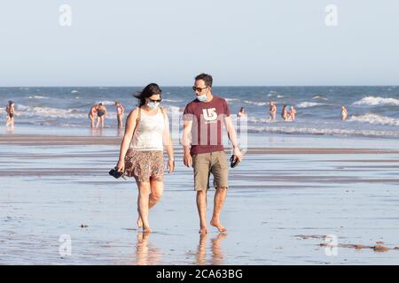 Punta Umbria, Huelva, Spain - August 2, 2020: Couple walking by the beach wearing protective or medical face masks. New normal in Spain with social di Stock Photo