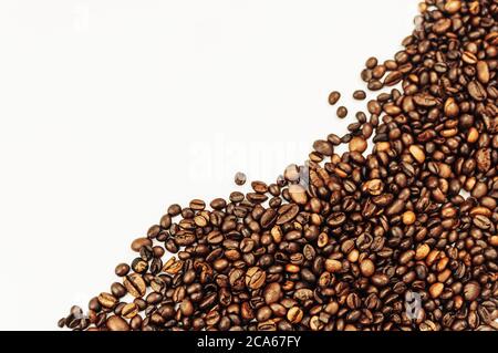 Coffee beans are scattered over the surface on a blank white background. a handful of brown coffee beans. Coffee background with copy space for Stock Photo