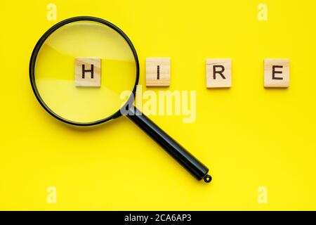 wooden letters blocks with word hire and magnifier on yellow background. Stock Photo